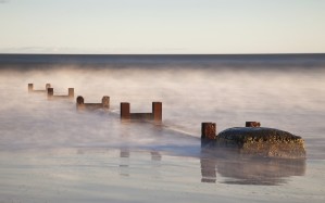 Wooden Posts And Boulders Immersed In Water At The Coast; Northumberland, England