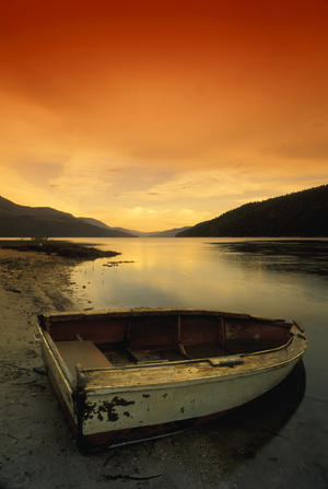 Old Rowboat At Water's Edge With Sunset Background