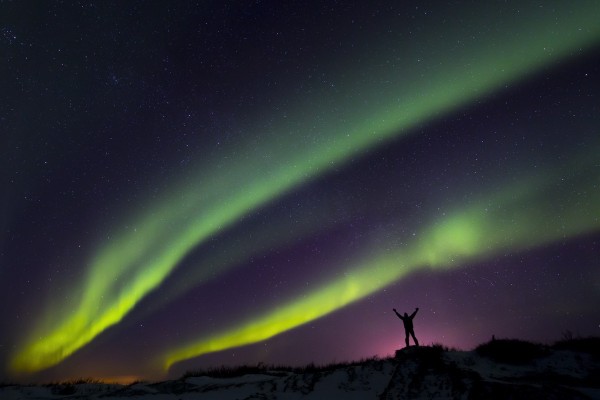 Colourful Aurora borealis over a man with arms outstretched silhouetted against light pollution from nearby Fort Greely; Alaska, United States of America by PacificStock