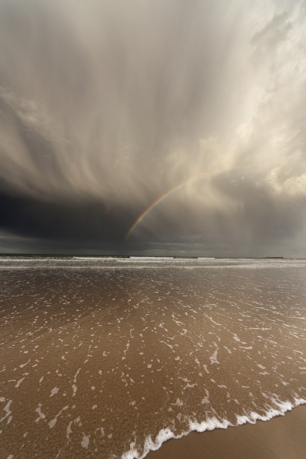 Tide Coming Up Onto The Beach With A Rainbow In The Clouds; Bamburgh, England by PacificStock