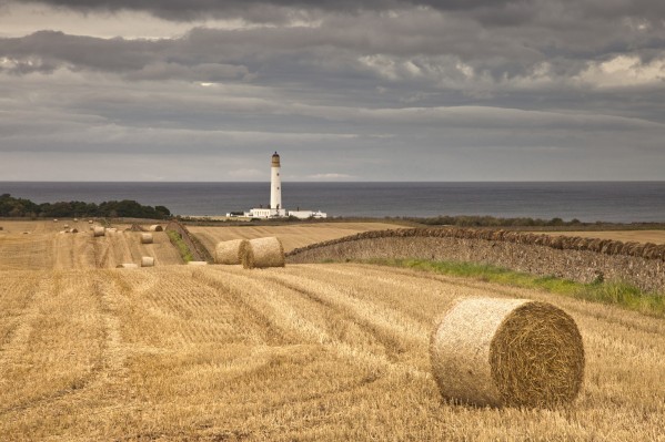 Barns Ness Lighthouse Along The Coast And Hay Bales In A Field In The Foreground; Lothian, Scotland by PacificStock