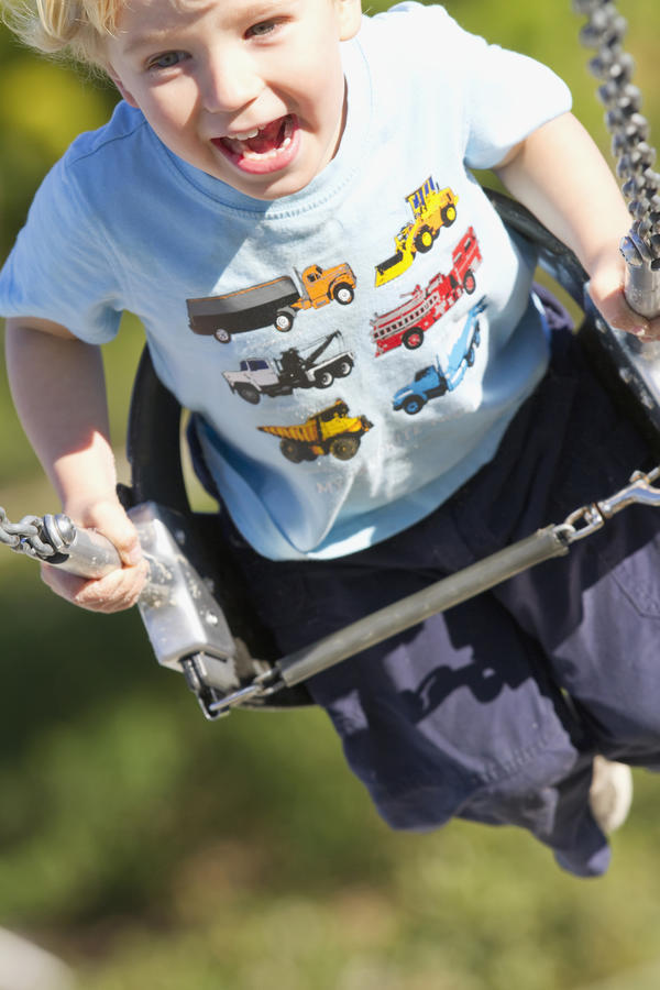 Young Boy Smiling Swinging In A Swing At The Playground. by PacificStock