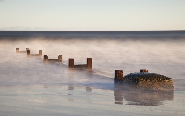 Wooden Posts And Boulders Immersed In Water At The Coast; Northumberland, England by PacificStock
