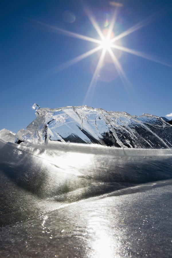 Ice Formations On A Frozen Lake Shoreline In The Mountains With A Sunburst And Blue Sky; Alberta, Canada by PacificStock