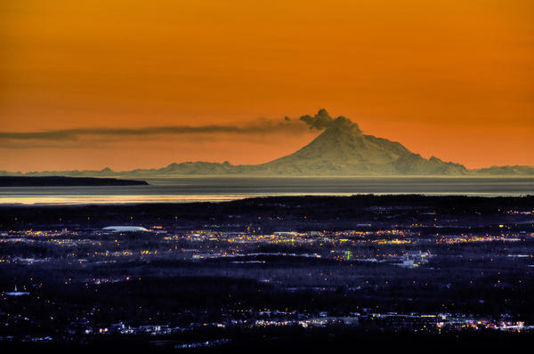 View Of The Anchorage Skyline At Sunset With Mount Redoubt Erupting In The Background, Southcentral Alaska Spring by PacificStock