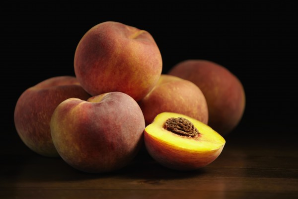 Peaches sitting on a wooden table, one cut in half; Montreal, Quebec, Canada by PacificStock