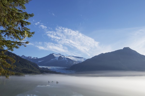 Three Kayakers paddle the shoreline of Mendenhall Lake as morning fog clears, Tongass National Forest, Juneau, Alaska. by PacificStock