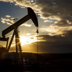 Silhouette of pump jack with dramatic storm clouds, blue sky and sunburst; Alberta, Canada