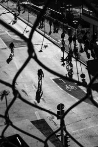 Black and white street photo of bicycles on a road in the city seen through a fence