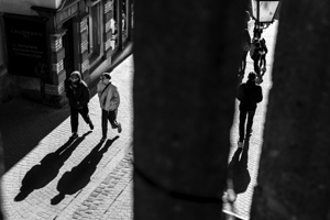 Black and white shot of people walking down a pedestrian street seen through a fence
