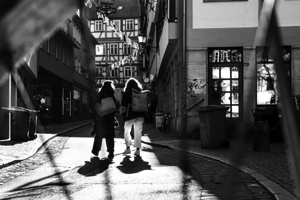 Black and white street photo of people walking down the road seen through the spokes of a bicycle