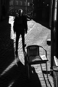 Black and white street photo of a man walking through a narrow alley 