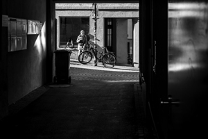 Black and white shot of older woman resting in the sun seen through a dark alleyway 