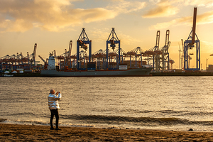 Man taking pictures at the Elbe River in Hamburg in front of harbor district at sunset