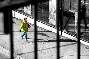 Selective colour black and white shot of a woman in a green coat walking down the street 