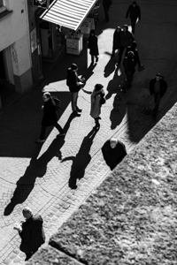 Black and white street photo of people walking and talking in an alley 