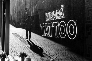 Black and white capture of the mirror image of a person reflected in a tattoo store window 