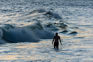 Lonely man walking in the waves at Ipanema Beach in Rio de Janeiro in Brazil at sunset  