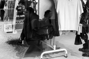 Black and white capture of mirror images of people reflected in a store window 
