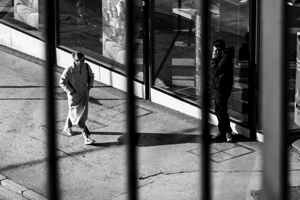 Black and white capture of a young woman walking down the street and looking at a man using his phone 
