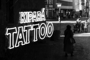 Black and white capture of the mirror image of an old woman and a family in the window of a tattoo studio  