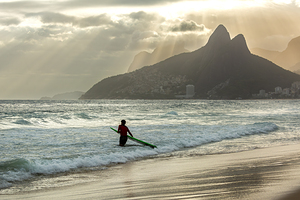 Surfer entering the water during dramatic sunset at Ipanema Beach in Rio de Janeiro 