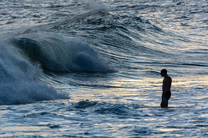 Lonely man standing in the waves at Ipanema Beach in Rio de Janeiro in Brazil at sunset  