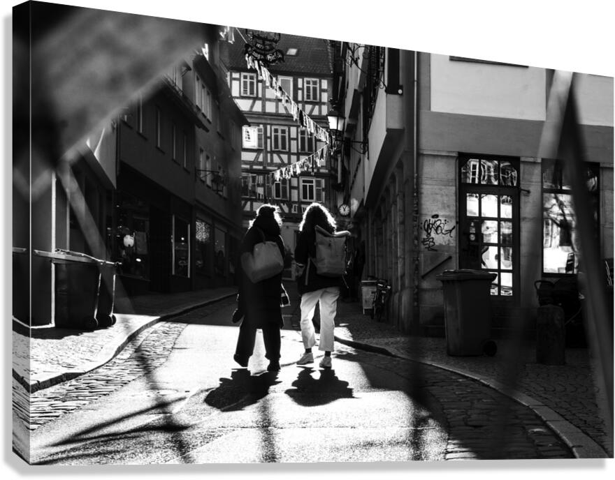 Black and white street photo of people walking down the road seen through the spokes of a bicycle Canvas Print