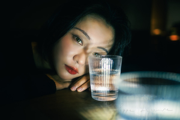 Young woman looking through a glass of water by Philippe Lejeanvre