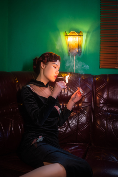 Young woman on a lether couch lighting a cigarett by Philippe Lejeanvre
