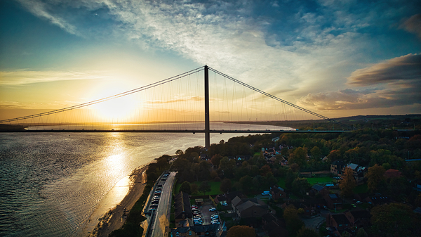Suspension bridge silhouette against a vibrant sunset over a tranquil river in Hull England. by Vasile Jechiu