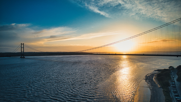Suspension bridge silhouette against a vibrant sunset sky with reflections on calm water in Hull England. by Vasile Jechiu