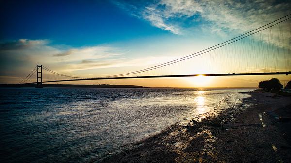 Suspension bridge silhouette at sunset with vibrant sky over calm river in Hull England. by Vasile Jechiu