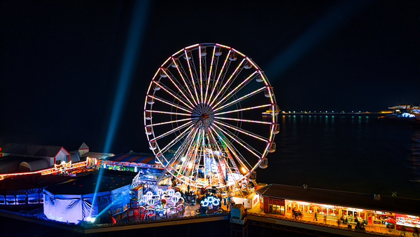 Illuminated Ferris wheel at night with vibrant lights and festive atmosphere at a seaside amusement park in Backpool England. by Vasile Jechiu