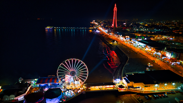 Aerial night view of a vibrant amusement park with illuminated Ferris wheel and tower by the seaside in Backpool England. by Vasile Jechiu