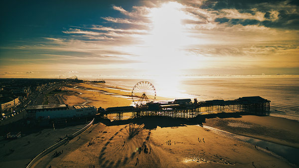 Aerial view of a beachfront with a pier and ferris wheel at sunset casting long shadows in Backpool England. by Vasile Jechiu