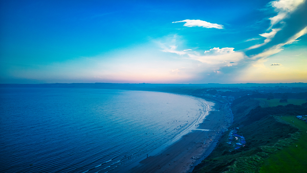 Scenic aerial view of a coastline at sunset with vibrant blue skies and a calm sea in Filey England. by Vasile Jechiu