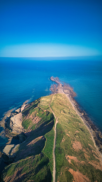 Aerial view of a scenic coastal landscape with a winding road leading to a headland against a blue ocean in Filey England. by Vasile Jechiu