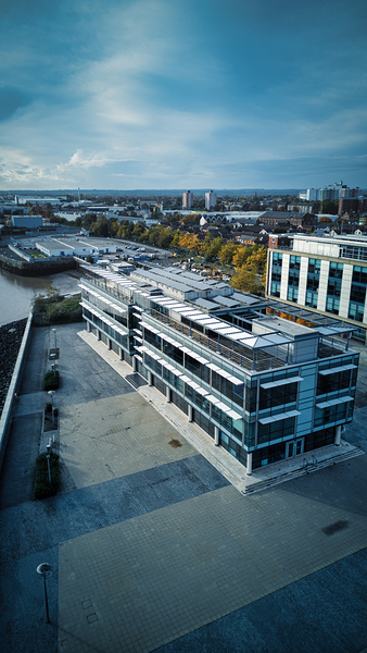 Modern office building with a rooftop terrace overlooking a river and cityscape under a cloudy sky in Hull England. by Vasile Jechiu