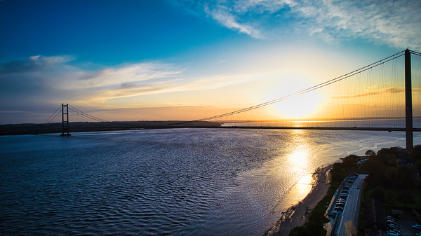 Sunset view over a calm river with a silhouette of a suspension bridge against a colorful sky in Hull England. by Vasile Jechiu