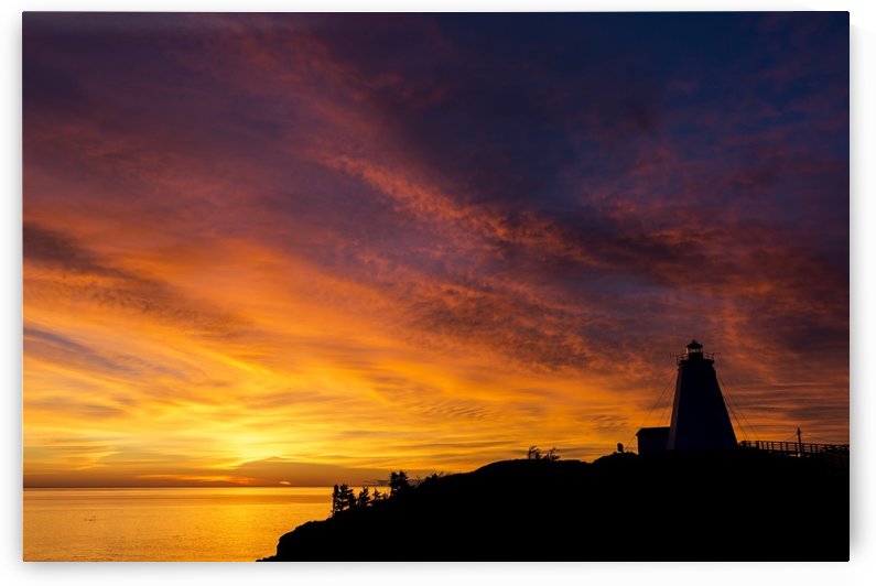 Silhouette of a lighthouse on a cliff overlooking a colourful reflected body of water with colourful dramatic clouds and blue sky; North Head, New Brunswick, Canada by PacificStock