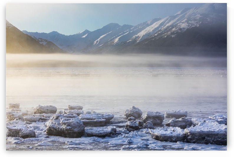 The sun shines through low altitude fog cast in warm light along Turnagain Arm and the Seward Highway, sea ice covering the ocean in the foreground, the Kenai Moutains revealed in the background, South-central Alaska; Alaska, United States of America by PacificStock