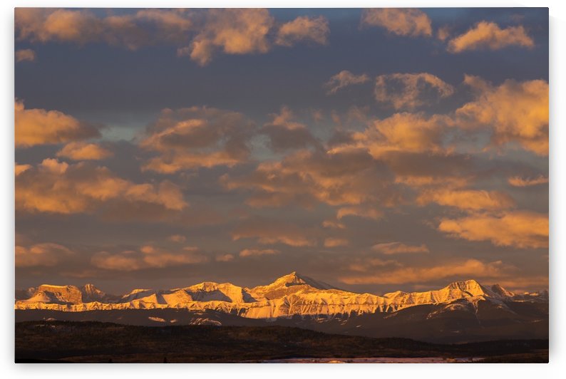 Glowing warmly lit snow covered mountain range and foothills with glowing clouds and blue sky at sunrise; Calgary, Alberta, Canada by PacificStock