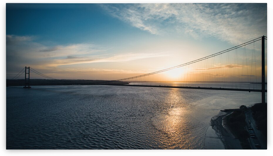 Sunset over a calm river with a silhouette of a suspension bridge against a colorful sky in Hull England. by Vasile Jechiu