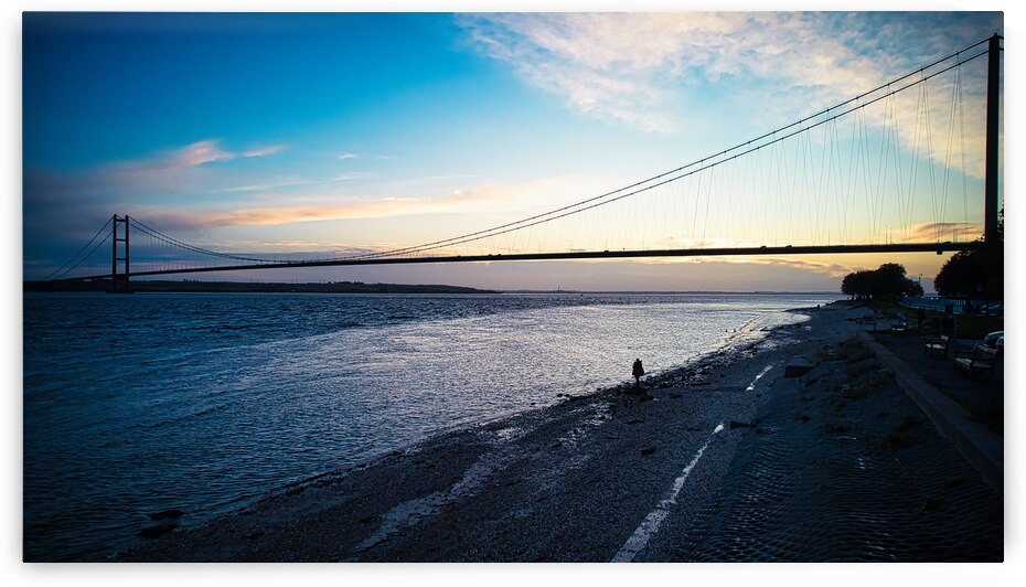 Scenic view of a suspension bridge over a tranquil river at dusk with silhouettes of people on the shore and a colorful sky in Hull England. by Vasile Jechiu