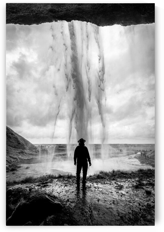 Man wearing hat standing behind waterfall in iceland by Gualtiero Boffi