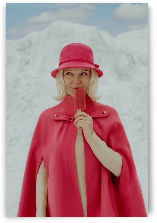 Vintage portrait of a blonde woman from the 1960s wearing a pink cape coat and cloche hat holding a popsicle in front of a mountain of snow in winter by Artmood Visualz