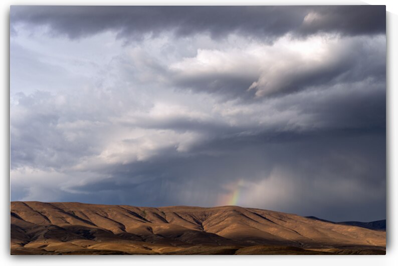 Rainbow with diagonal clouds over morning light on mountains by Lisa von Biela