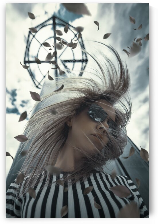 Young blonde woman wearing aviator style sunglasses and a black and white striped shirt her hair swirling in the wind in front of a tower with autumn leaves flying around by Artmood Visualz