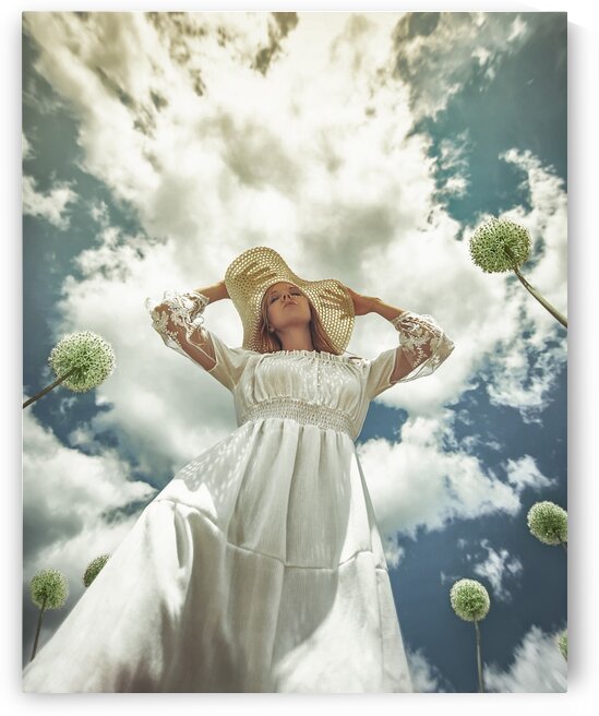 Ground angle view of a young blonde woman in a white dress with a white hat surrounded by dandelions under a blue sky with white clouds by Artmood Visualz
